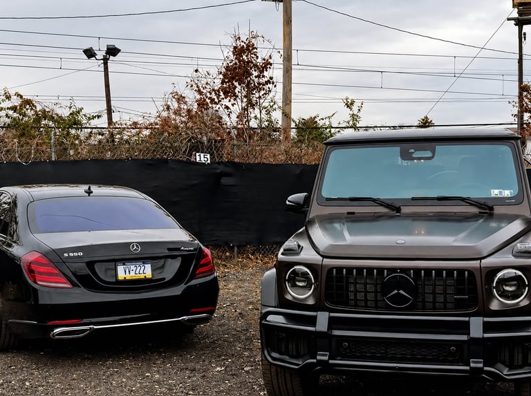 Two luxury vehicles parked side by side: a black Mercedes sedan on the left and a black Mercedes SUV with distinctive round headlights on the right