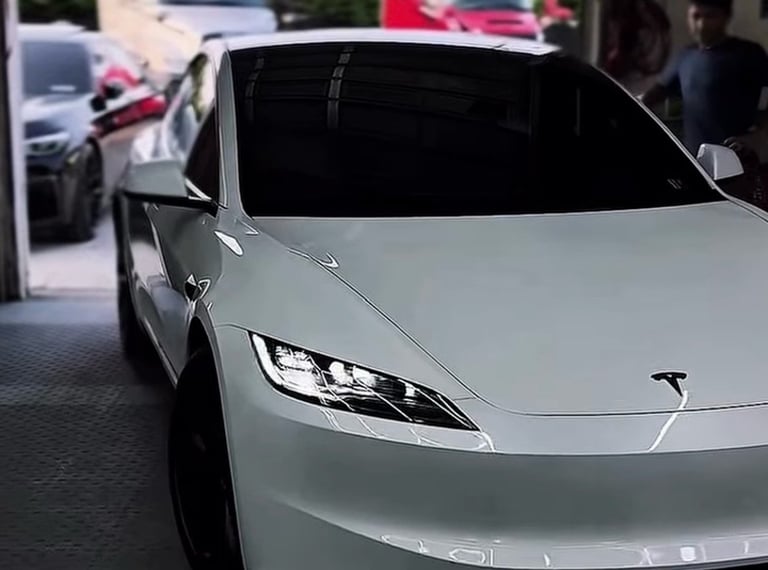 White Tesla electric vehicle parked indoors, front angle view showing LED headlights and sleek design