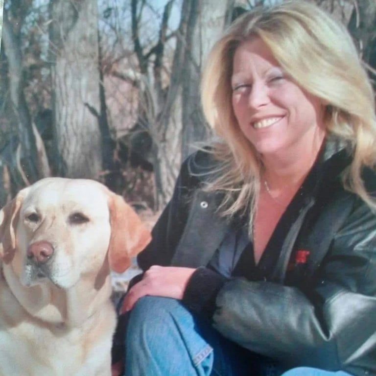 Woman with blonde hair smiling while posing with a yellow Labrador retriever outdoors