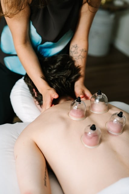 Cat performing cupping therapy with glass cups on a client's back