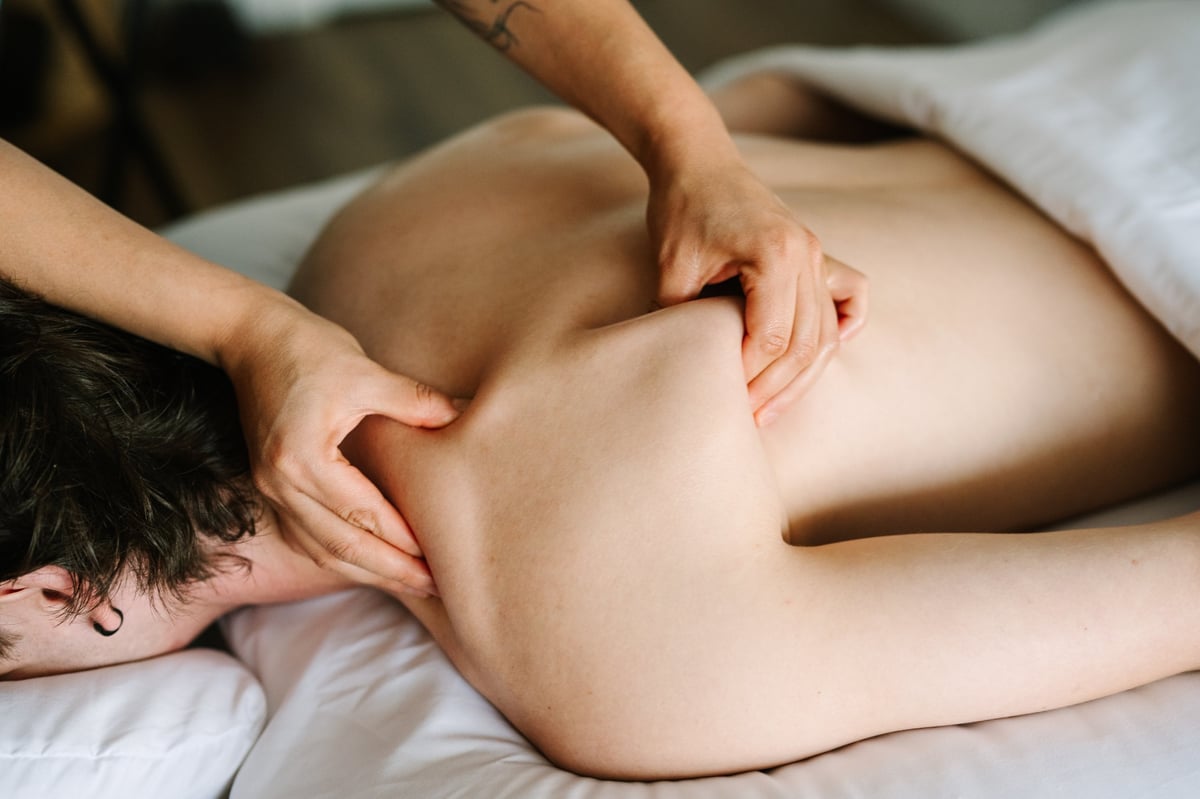 Therapist performing a deep tissue massage on a client's back and shoulder while lying face down on a massage table