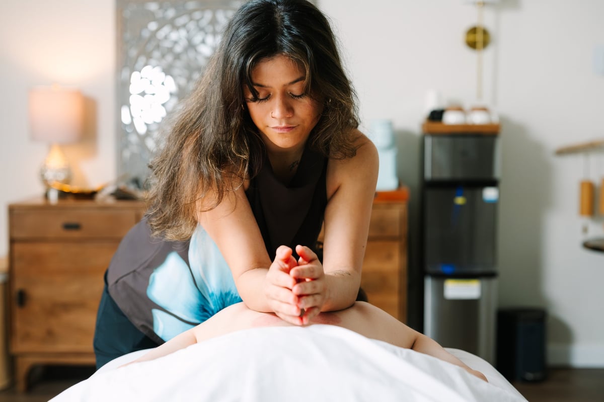 Woman performing massage or physical therapy on a patient lying down in a bedroom setting