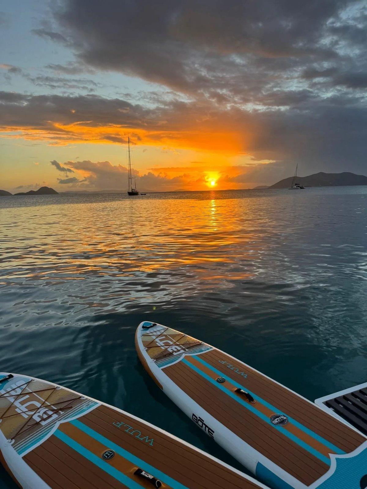 Allegra — SUP boards in foreground with sailboats anchored in bay at sunset
