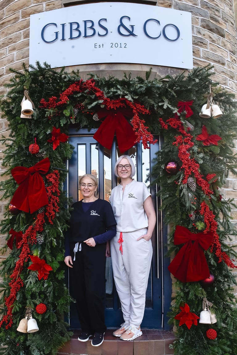 Two women standing in doorway of Gibbs & Co shop entrance decorated with red and green Christmas garland and bows