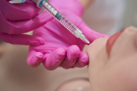 Healthcare worker in magenta gloves holding a syringe administering an injection to a patients arm