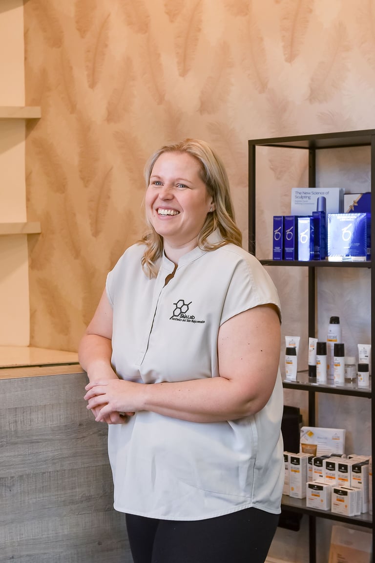 Woman in light gray uniform smiling in a spa or salon interior with product shelving and tan textured walls