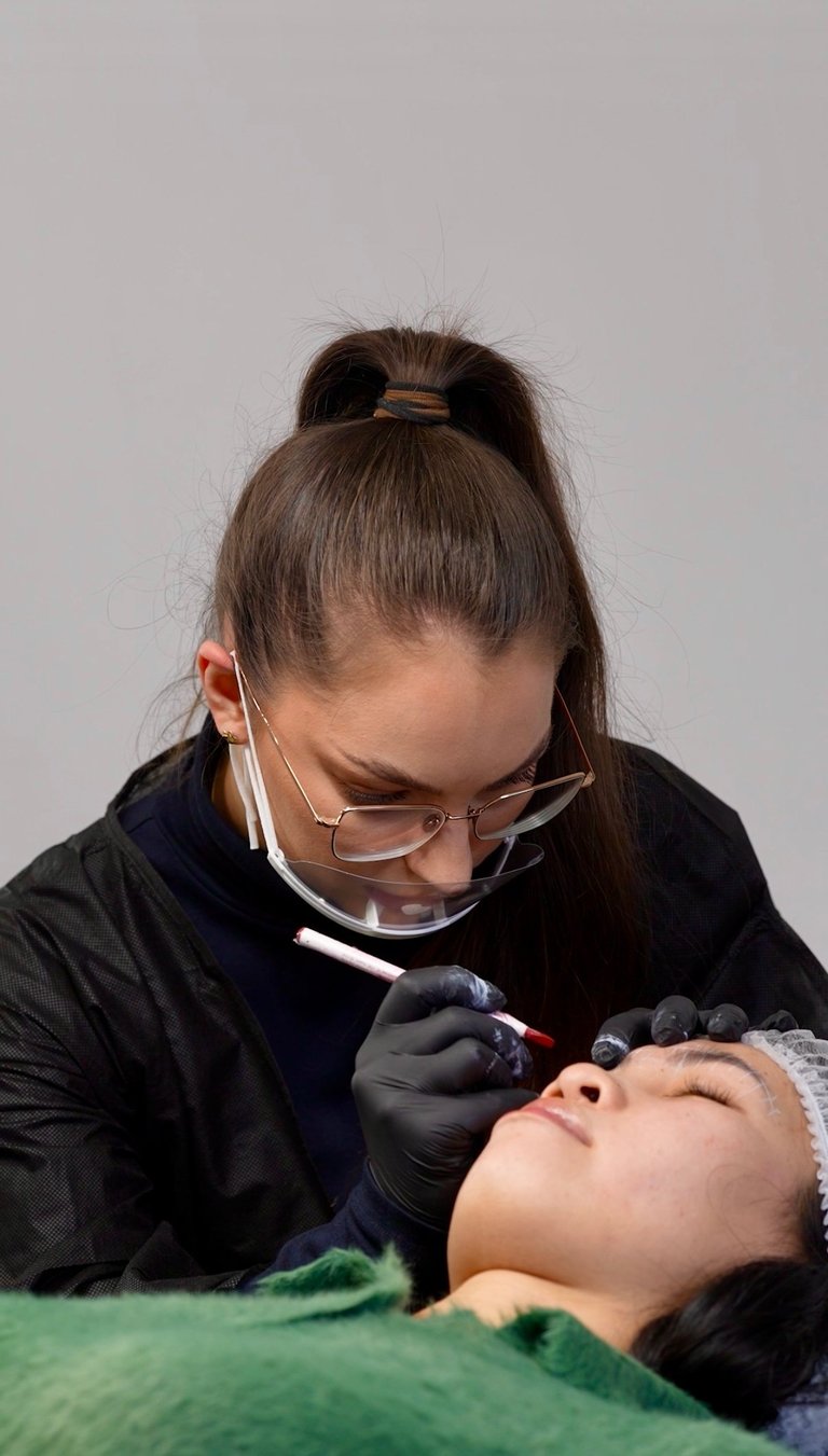 Permanent makeup artist wearing protective eyewear and glasses applying microblading to a clients eyebrow