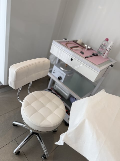 Modern beauty salon workstation with white quilted stool, desk with pink top, equipment, and cosmetic products