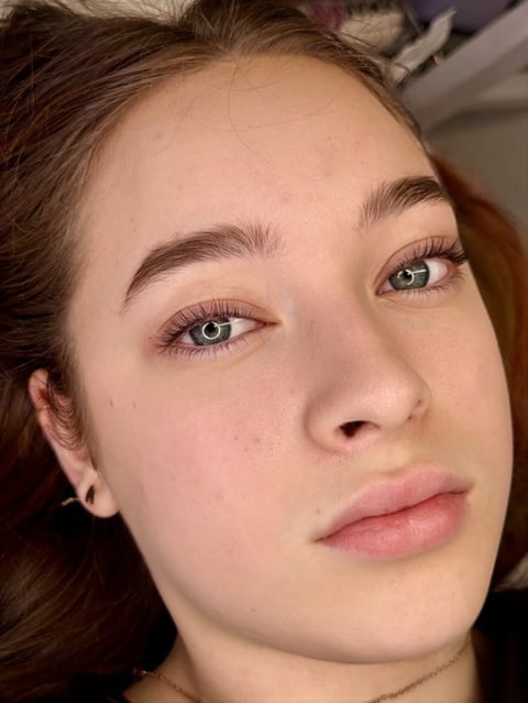 Close-up portrait of a woman with brown hair, defined eyebrows, and natural makeup looking at the camera