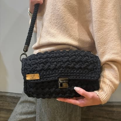 Person holding a black crocheted clutch bag with a gold clasp and woven strap