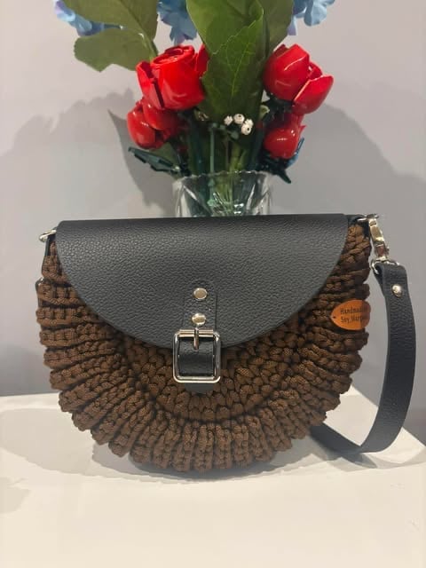 Brązowa pleciona torebka crossbody Oreo z szarą skórzaną klapą i srebrną klamrą, w tle czerwone i niebieskie kwiaty.