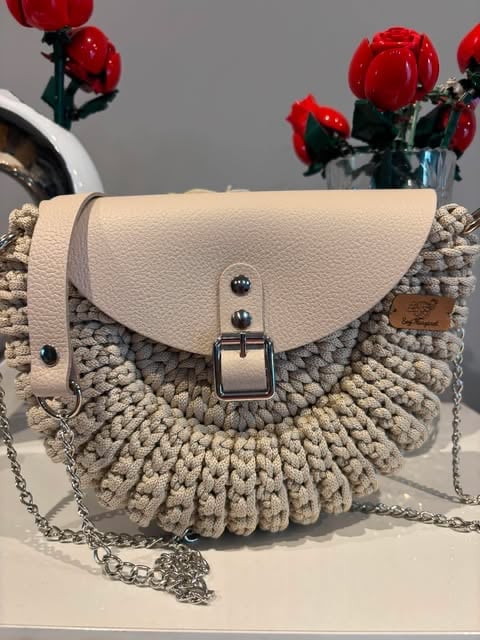 Kremowo-beżowa pikowana torebka crossbody Oreo ze skórzaną klapką i srebrnym łańcuchem, w tle czerwone kwiaty.