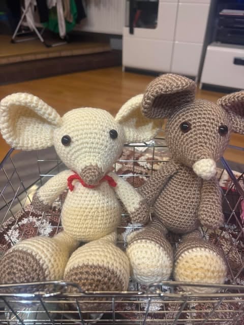 Dwie szydełkowe myszki amigurumi — kremowa z czerwoną kokardką i beżowo-szara, w drucianym koszyku.