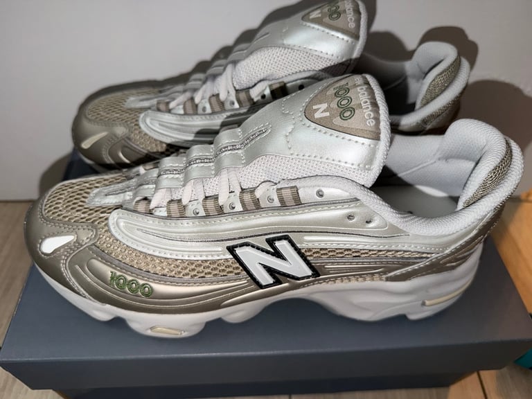 New Balance 1000 white sneakers with black stripes on a blue box
